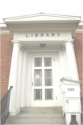facade of old library building; white columns and portico against red brick with gray cement steps and a large, glass-paned entry door
