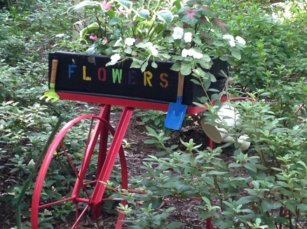 Picture: Old red bike with cart made into a flowerbox full of blooms: Beauty is crafted from everyday elements.
