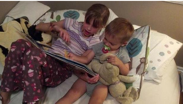 big sister holds book and reads to little brother hoding a stuffed rabbitPicture