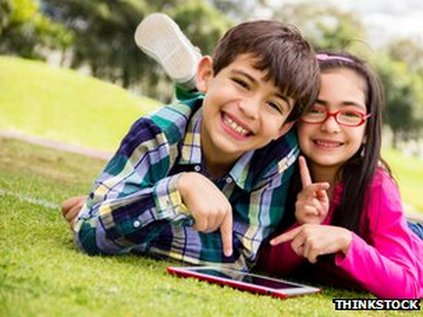 Children's e-books: a boy and girl are outside on the grass, lying on their tummies, reading an e-book