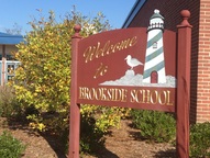 Tips for Kid Lit Author Visits ~School welcome sign against red brick building and shrubs