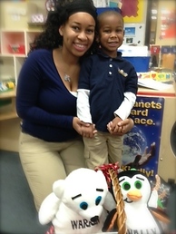 Smiling first-grader and mom kneel next to the Wallie and Warren goody basket he won in a school coloring contest